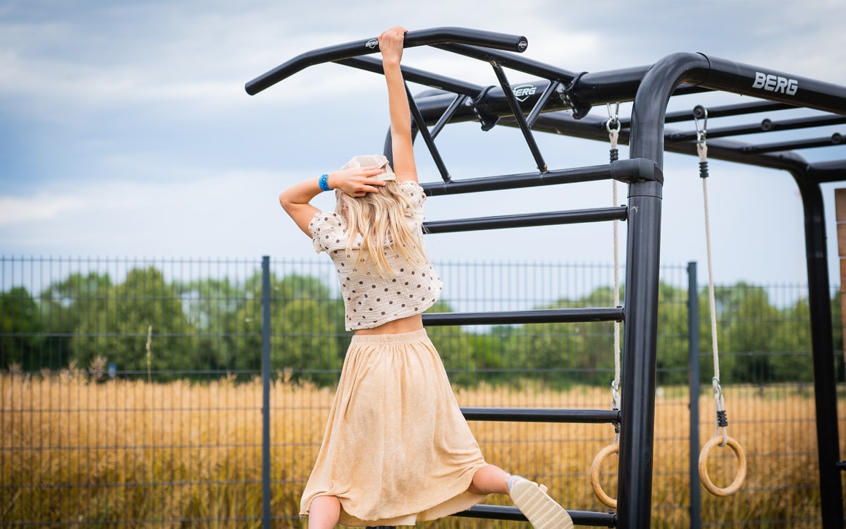 Ein Mädchen macht Akrobatikübungen an der PlayBase Klimmzugstange.
