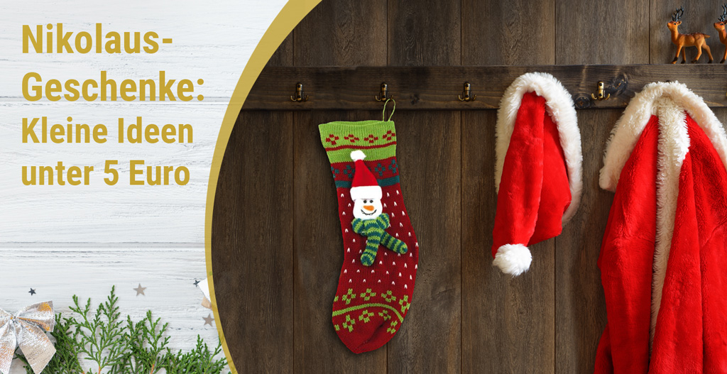 Eine Nikolaus-Socke hängt an einer Wand. Daneben eine Nikolausmütze und ein roter Umhang mit weißem Fellbesatz.