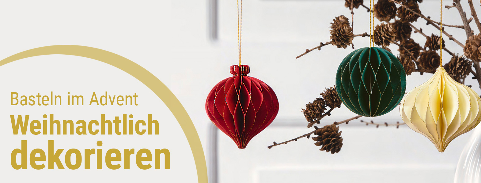 Drei Wabenbälle Christmas von Folia hängen an einem Trockengesteck als Winterdekoration in den Farben Rot, Grün und Creme.