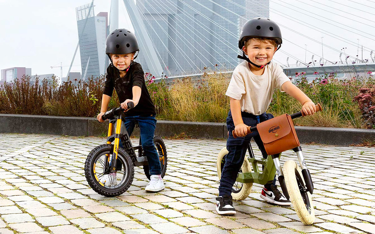 Zwei kleine Kinder fahren mit BERG Biky Laufrädern umher. Eines auf einem Biky Cross, das andere auf einem Biky Retro mit Ledertasche. Beide tragen zu ihrer Sicherheit einen Fahrradhelm.