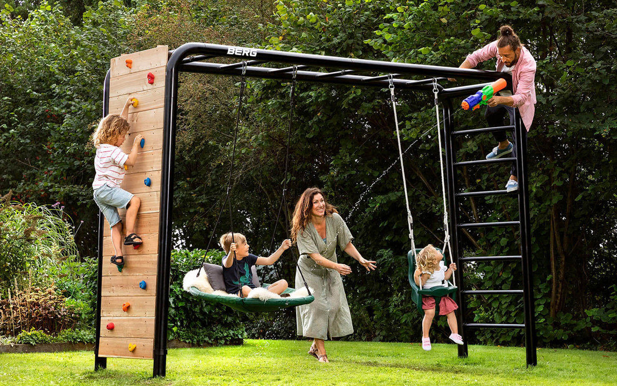 Eine Familie spielt gemeinsam auf der PlayBase mit Kletterwand, Nestschaukel und Babysitz.