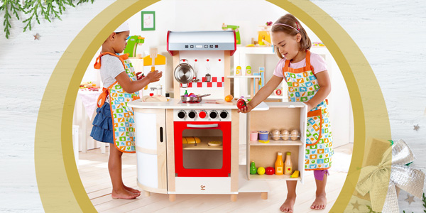 Hape Küchentraum: 2 Mädchen spielen mit der Spielküche aus Holz in Verkleidung als kleine Köchinnen.