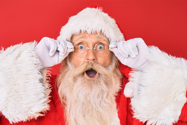 Weihnachts-Mann vor rotem Hintergrund mit erstauntem Gesichtsausdruck, der sich an seine Brille fasst.